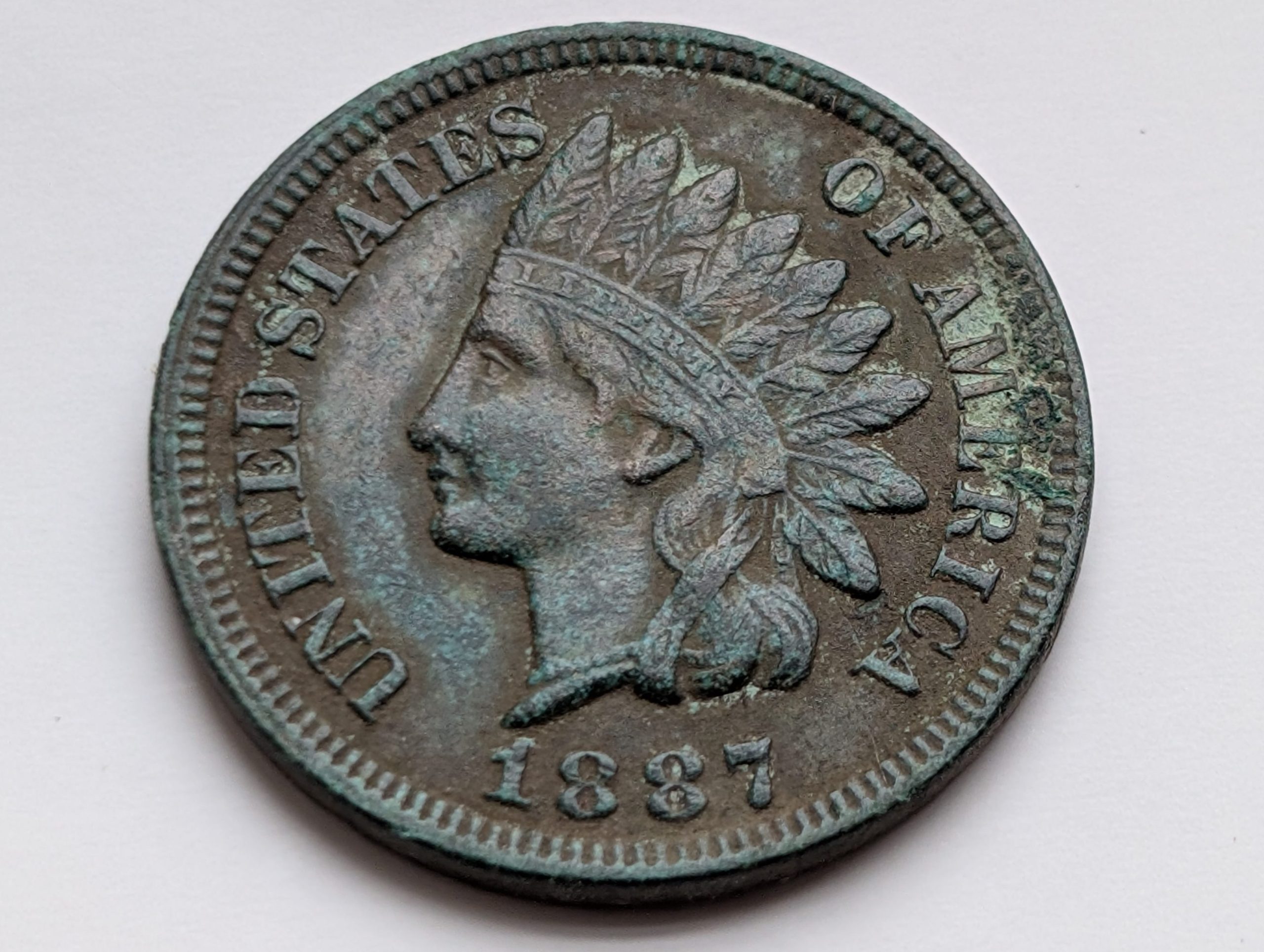 Heavily corroded 1887 Indian Head cent with thick green verdigris and severe surface pitting covering much of the obverse.