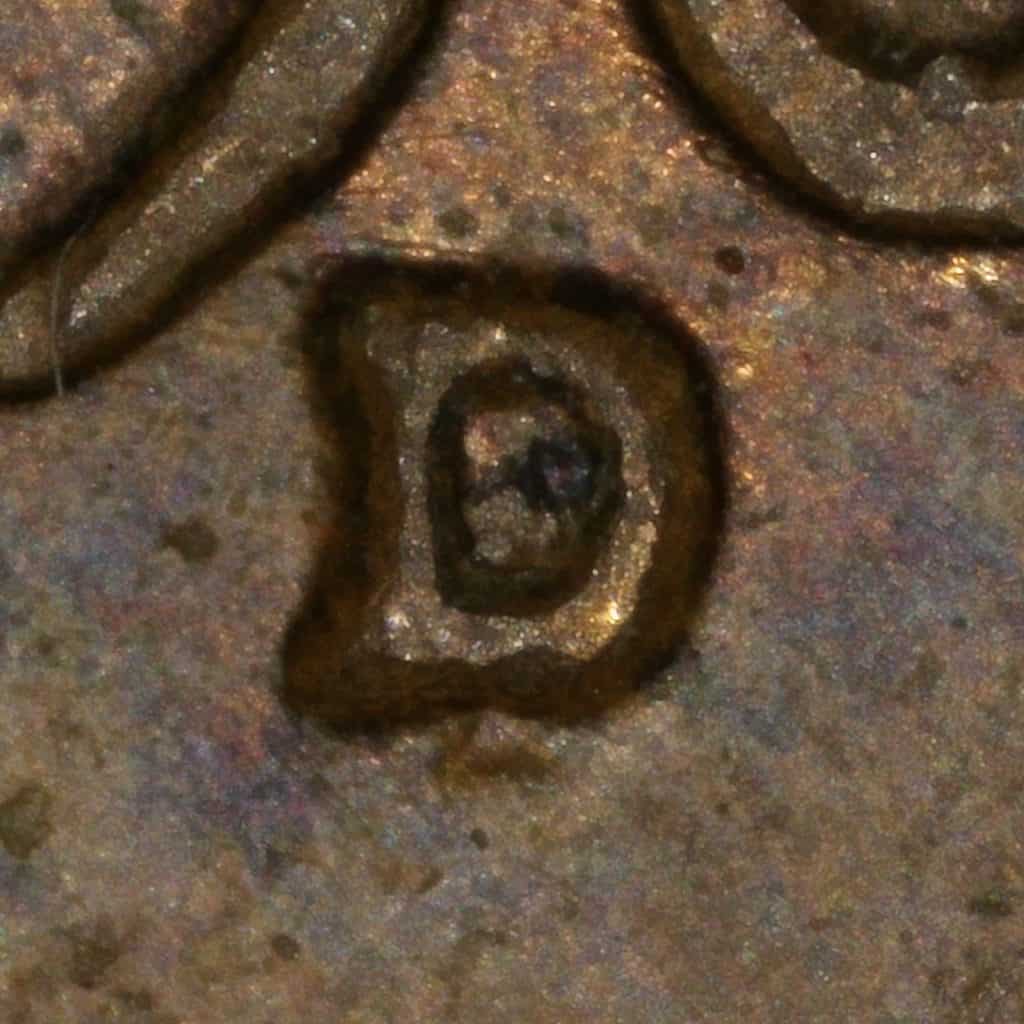 Extreme close-up of the D mintmark on a 1961-D Lincoln cent showing internal separation and secondary contours from repunching.