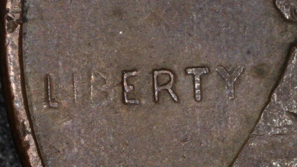 Magnified view of the word LIBERTY on a 1996 Lincoln cent showing missing and weak letter details from a grease-filled die.